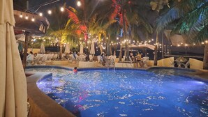 A pool area with lounge chairs and umbrellas, surrounded by palm trees and string lights. - Treasure Island Resort (Olongapo)