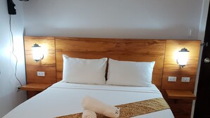 A neatly made bed with a patterned throw, two bedside lamps, and a wall-mounted fan. - Treasure Island Resort (Olongapo)