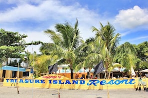 A banner welcoming to Treasure Island Resort with palm trees and buildings in the background. - Treasure Island Resort (Olongapo)