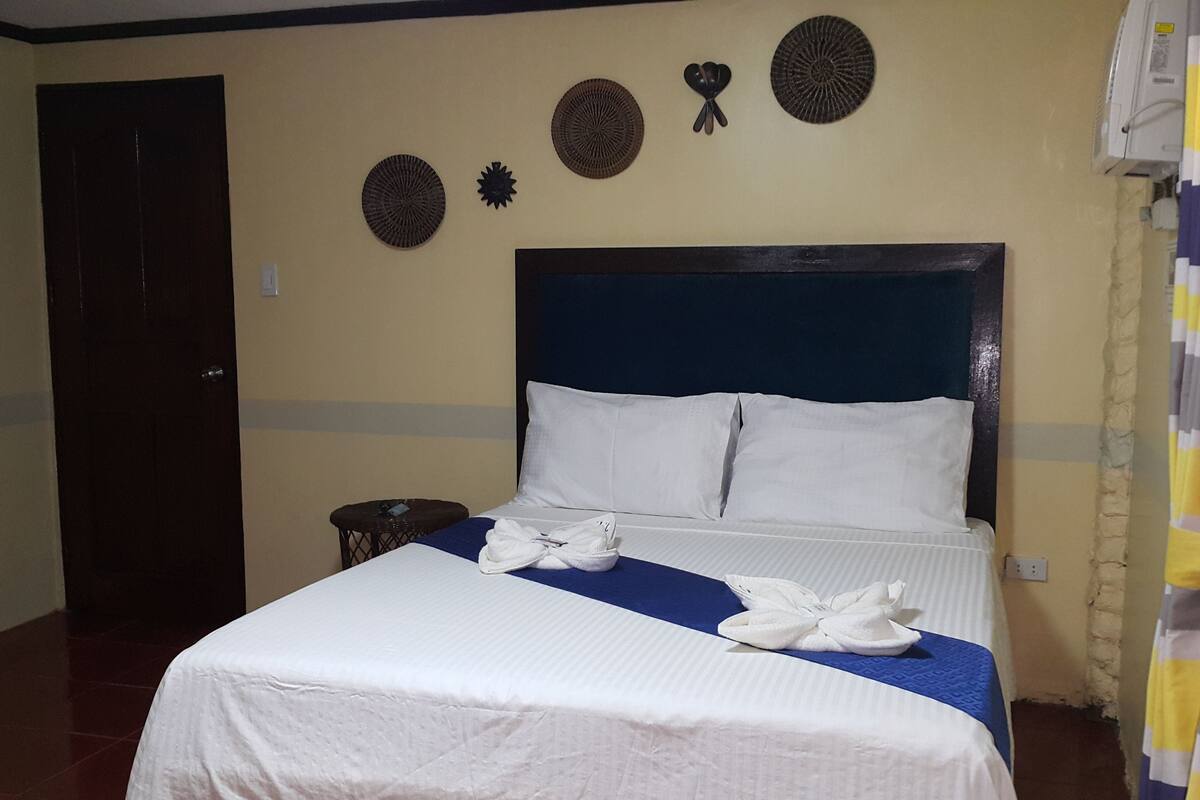 A hotel room with a bed, a small table, decorative wall art, and a curtain.