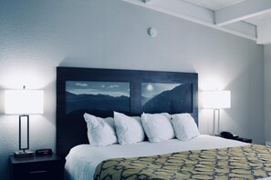 A hotel room with a large bed, two bedside lamps, a nightstand with a phone, and a headboard with a mountain view painting. - Baymont by Wyndham Cookeville (Cookeville)