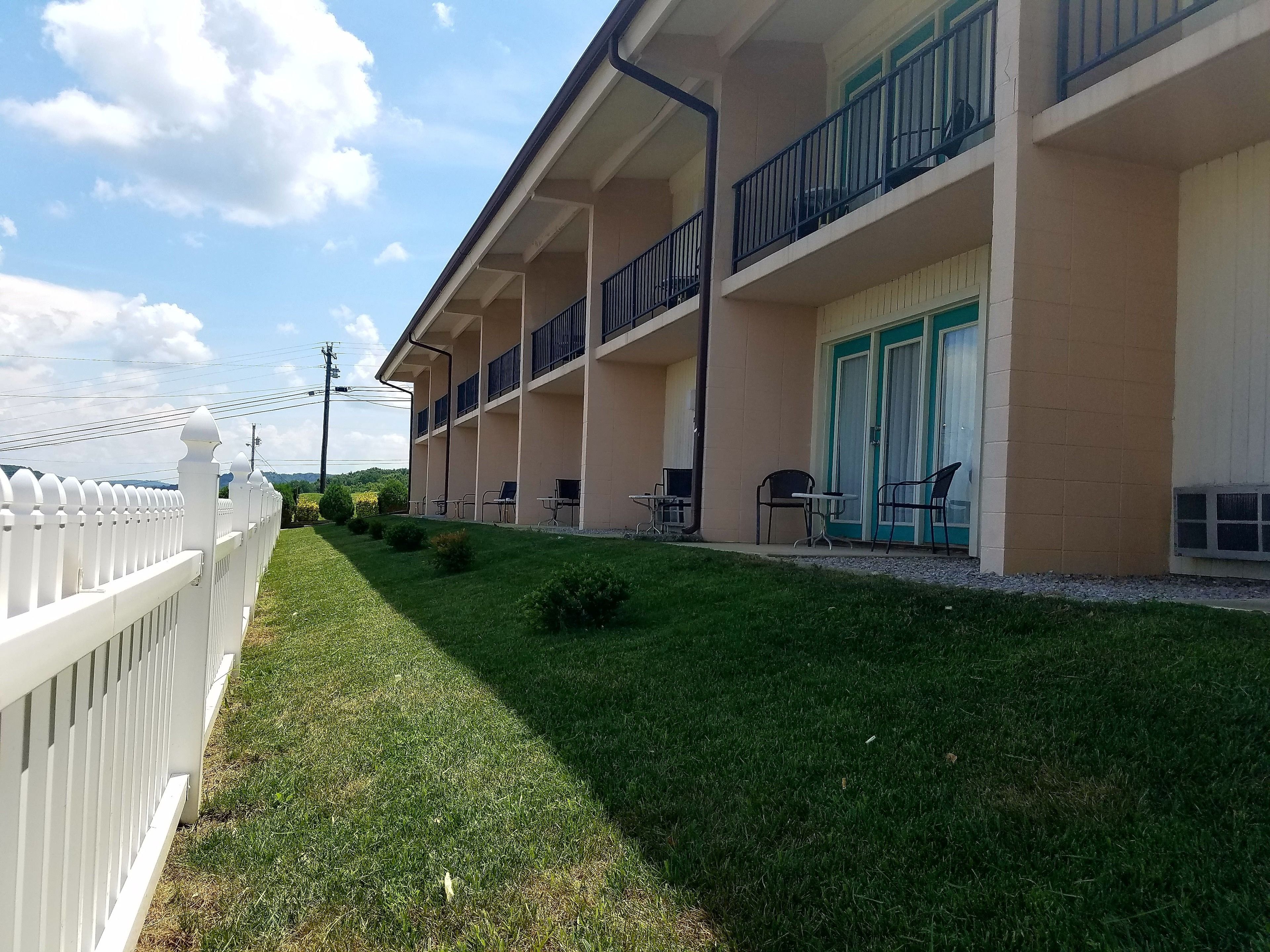 A hotel with a white fence, a well-maintained lawn, outdoor seating, and a balcony with railings.