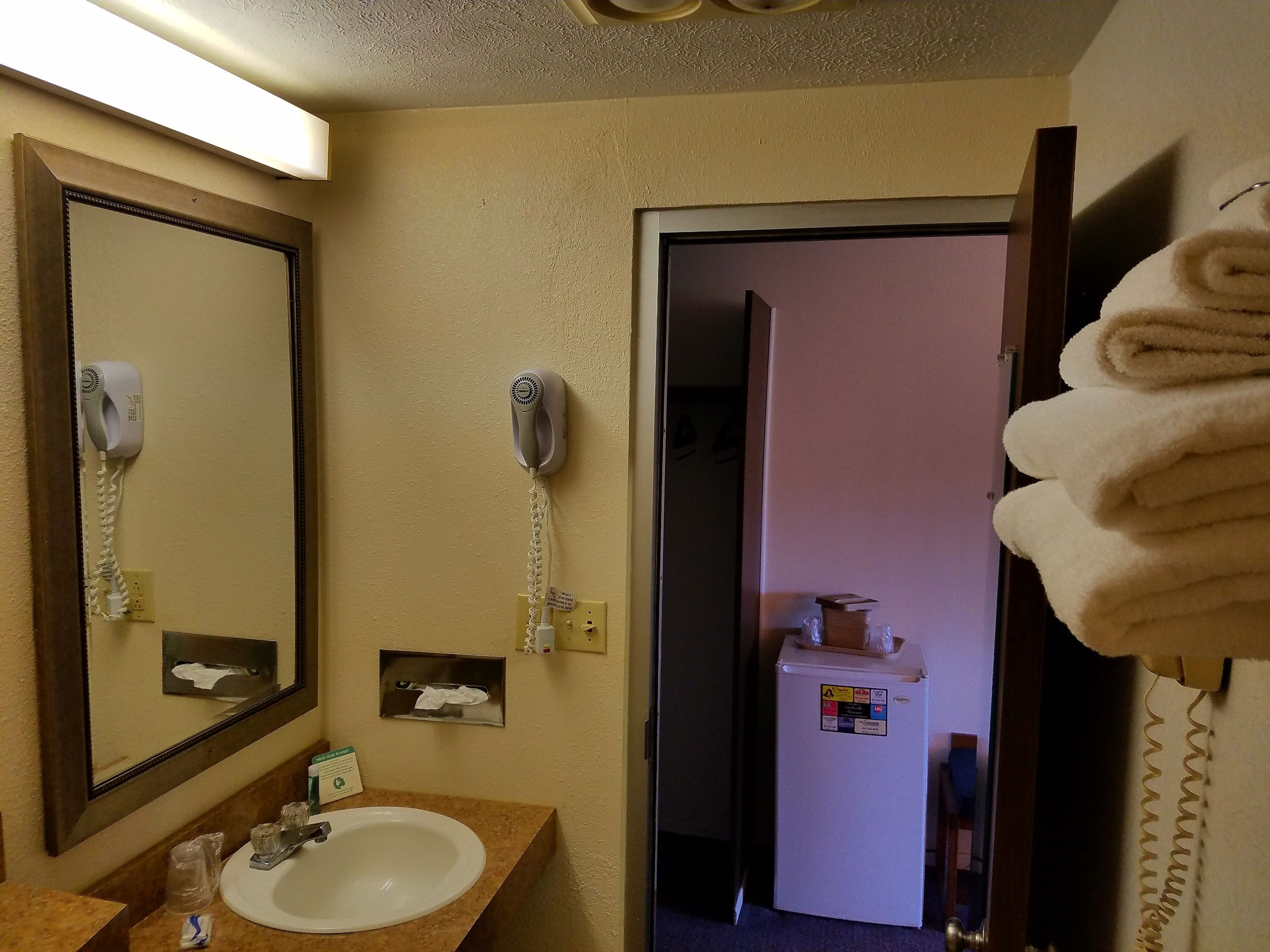 A hotel bathroom with a sink, two hair dryers, a mirror, and a towel rack.