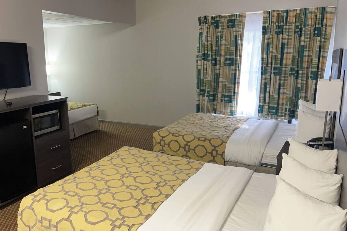 Une chambre d’hôtel avec deux lits, une télévision, un bureau et une fenêtre avec des rideaux.
