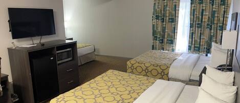 Habitación de hotel con dos camas, televisión, escritorio y ventana con cortinas.