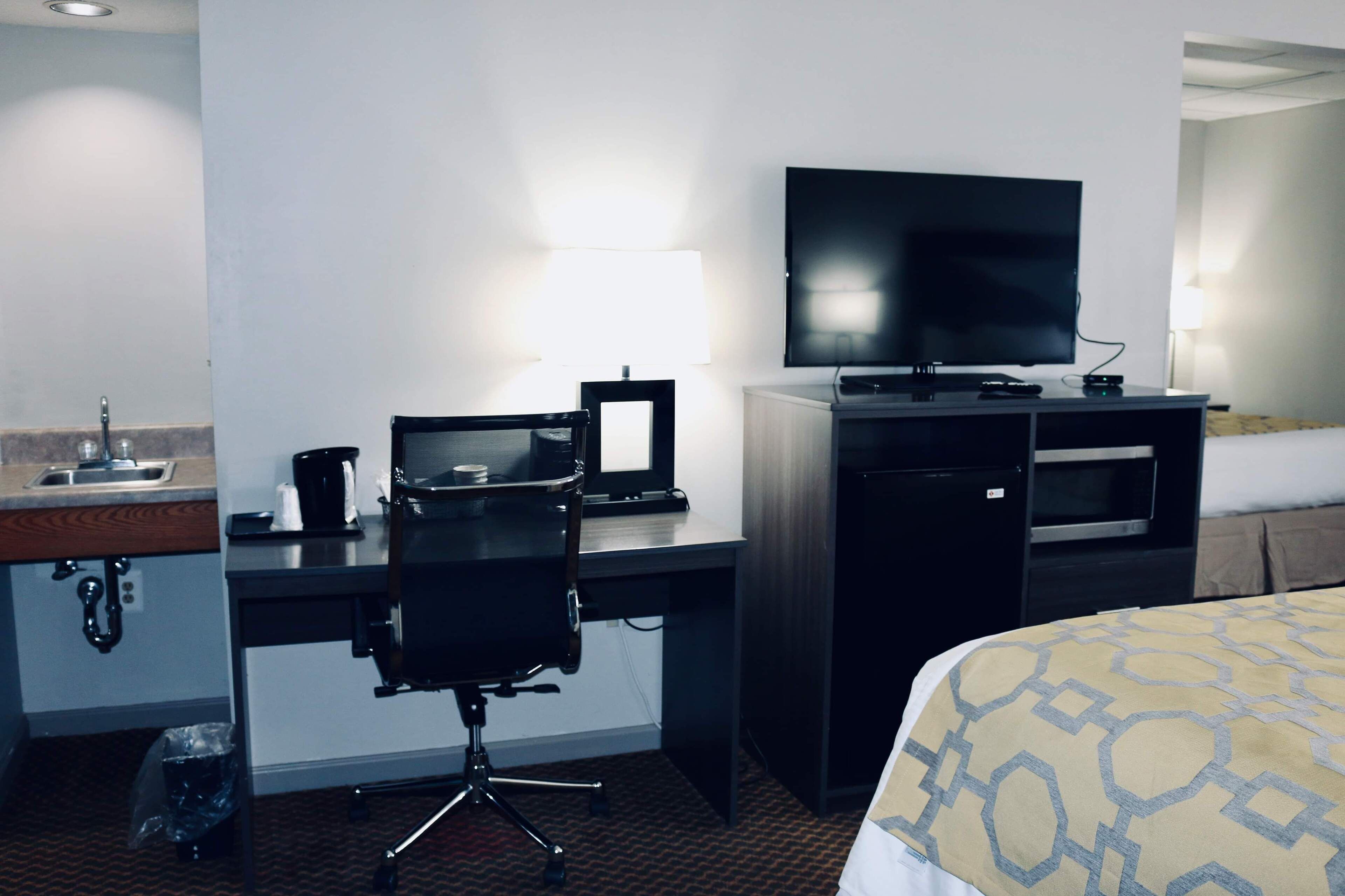 Une chambre d’hôtel équipée d’un lit, d’un bureau avec un ordinateur, d’une télévision, d’une lampe et d’un mini-bar.