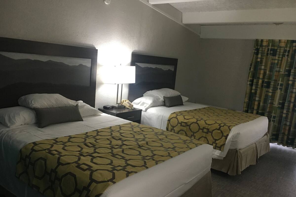 Une chambre d’hôtel avec deux lits, une table de chevet avec une lampe et un téléphone, et une fenêtre avec des rideaux.
