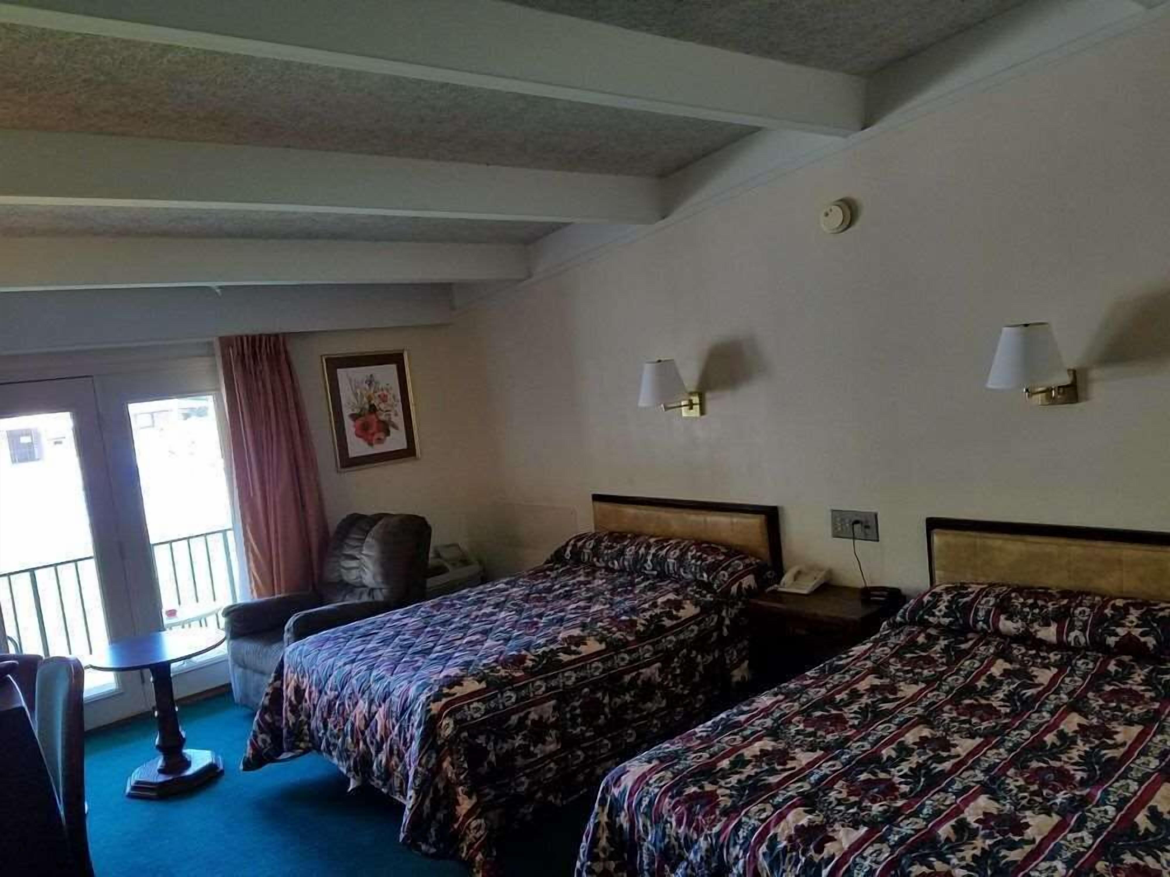 A hotel room with two beds, a desk, a chair, a lamp, and a picture on the wall.