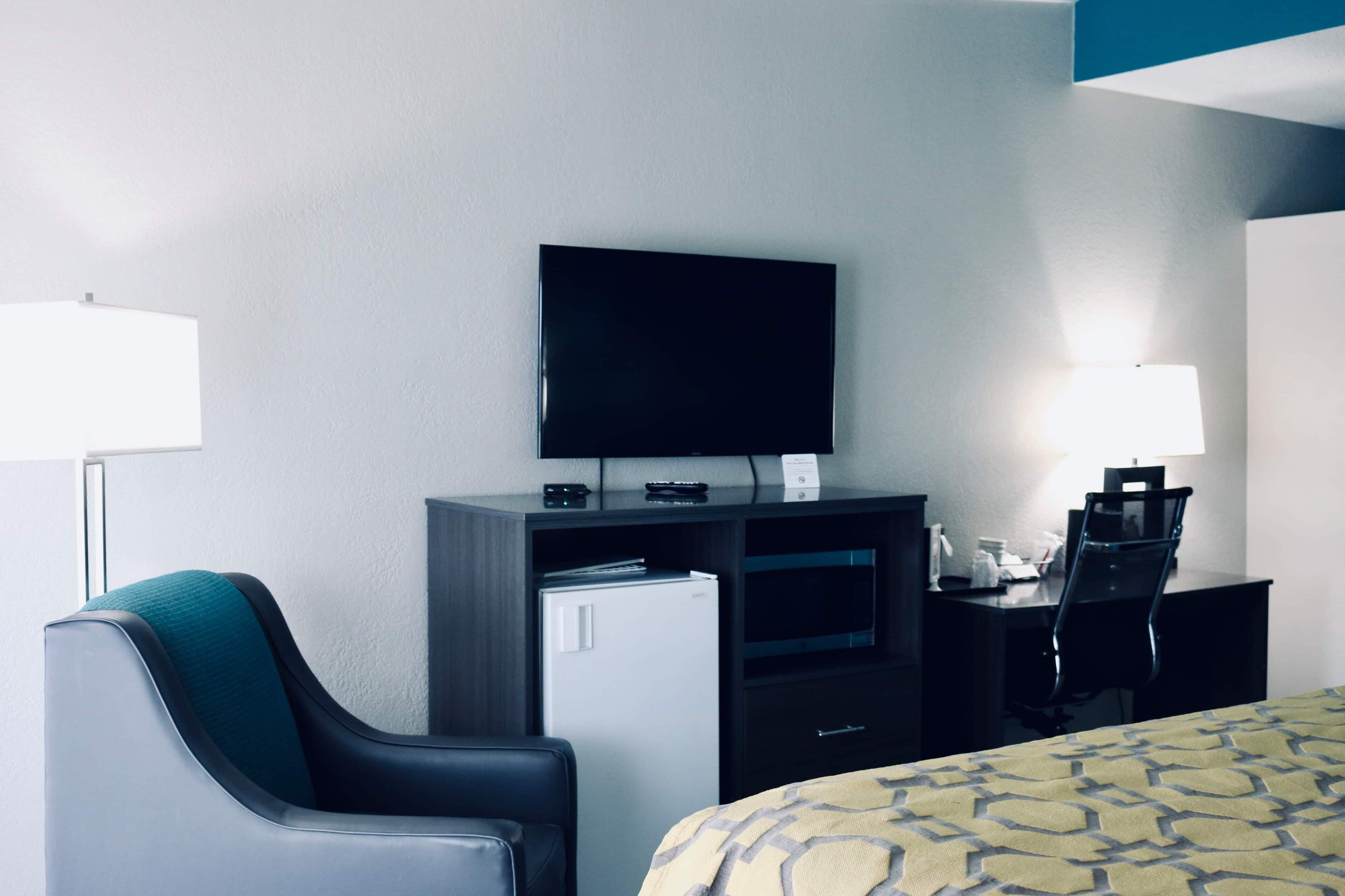 A hotel room with a bed, a desk with a computer, a television, a refrigerator, and a chair.
