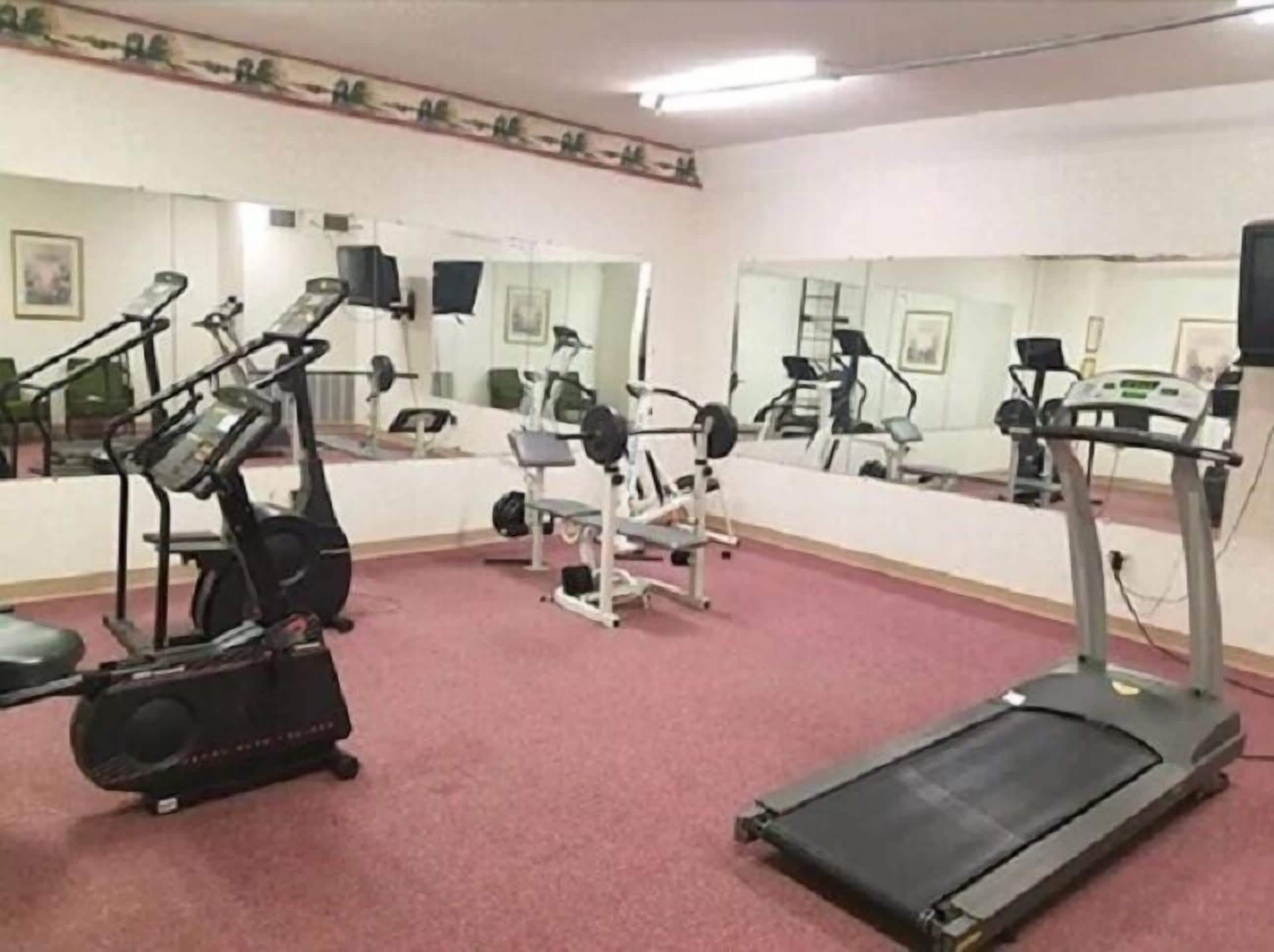 A gym with exercise equipment, including treadmills and weight machines, and mirrors on the walls.