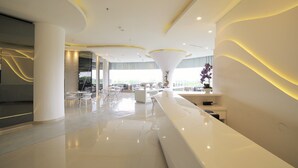 Un moderno vestíbulo de hotel con un diseño elegante en blanco, que incluye un mostrador de recepción central, una amplia zona de estar y grandes ventanales que ofrecen luz natural.