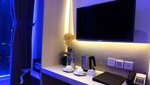 Ein Hotelzimmer mit Schreibtisch, Stuhl, Wand-Fernseher, Blumen in einer Vase, Kaffeemaschine, Telefon und Tablet.