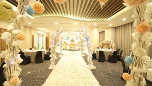 Un vestíbulo de hotel con un pasillo central que conduce a la recepción, decorado con arreglos florales y suelo alfombrado.