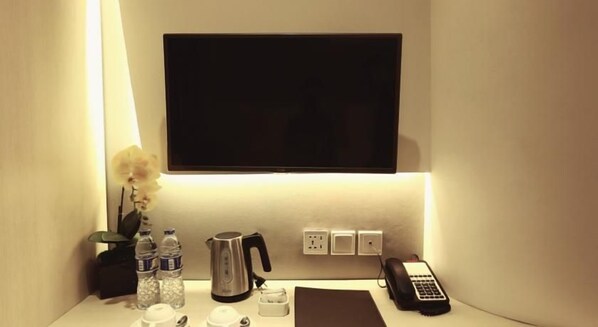 Habitación de hotel con televisor de pantalla plana sobre un escritorio, una tetera, un teléfono y un jarrón con flores.