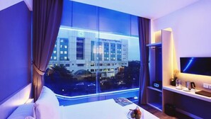 Habitación de hotel con un ventanal grande, una cama, un televisor y una mesita con una bandeja de frutas.