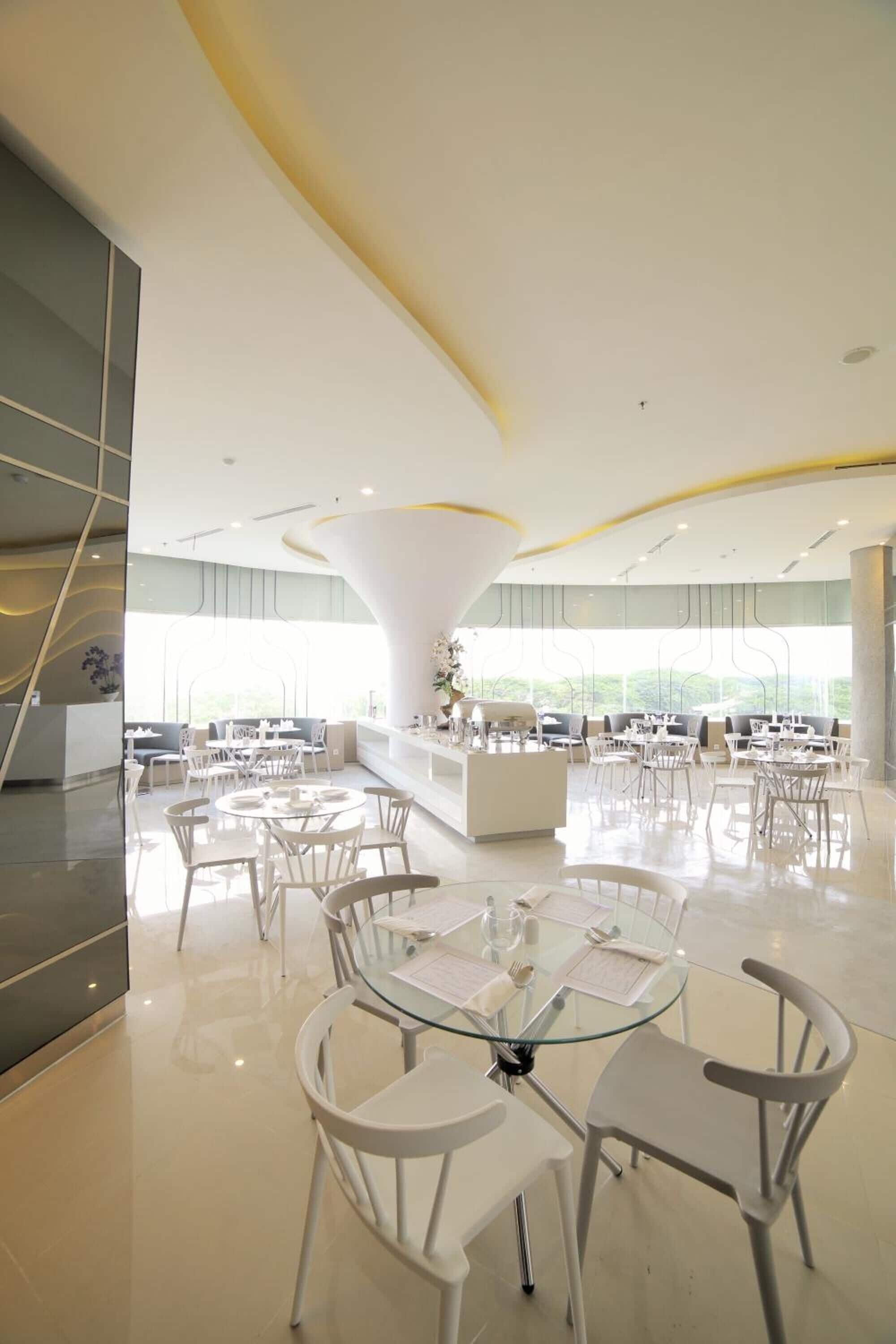 A modern dining area with round tables and white chairs, large windows, and a central white pillar.
