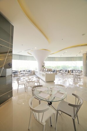 Un comedor moderno con mesas redondas y sillas blancas, ventanas amplias y un pilar blanco central.