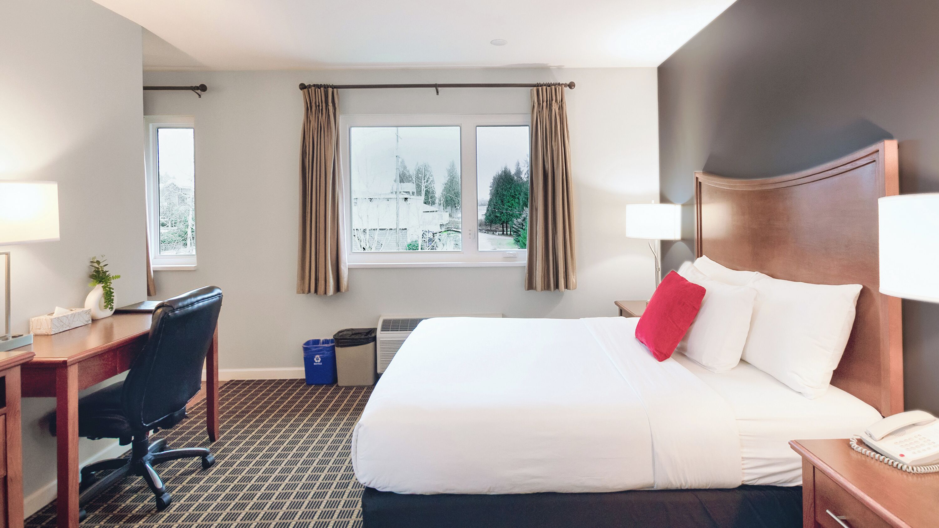 Habitación de hotel con una cama grande, un escritorio, una silla, una lámpara y una ventana con cortinas.