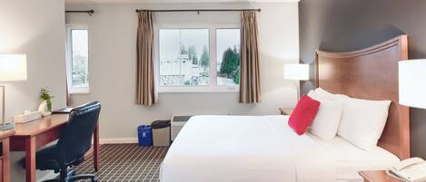 Habitación de hotel con una cama grande, un escritorio, una silla, una lámpara y una ventana con cortinas.