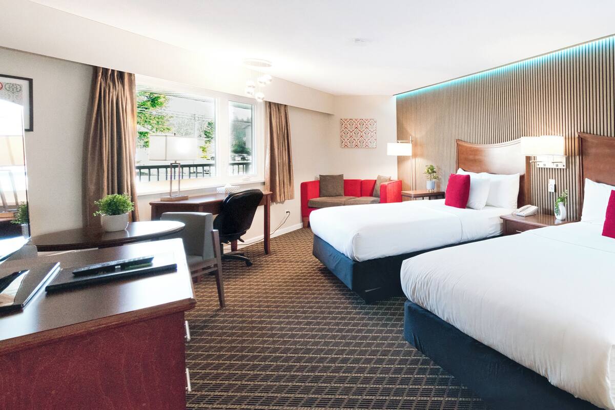 Ein Hotelzimmer mit zwei Betten, einem Schreibtisch, einem Stuhl und Blick ins Freie.