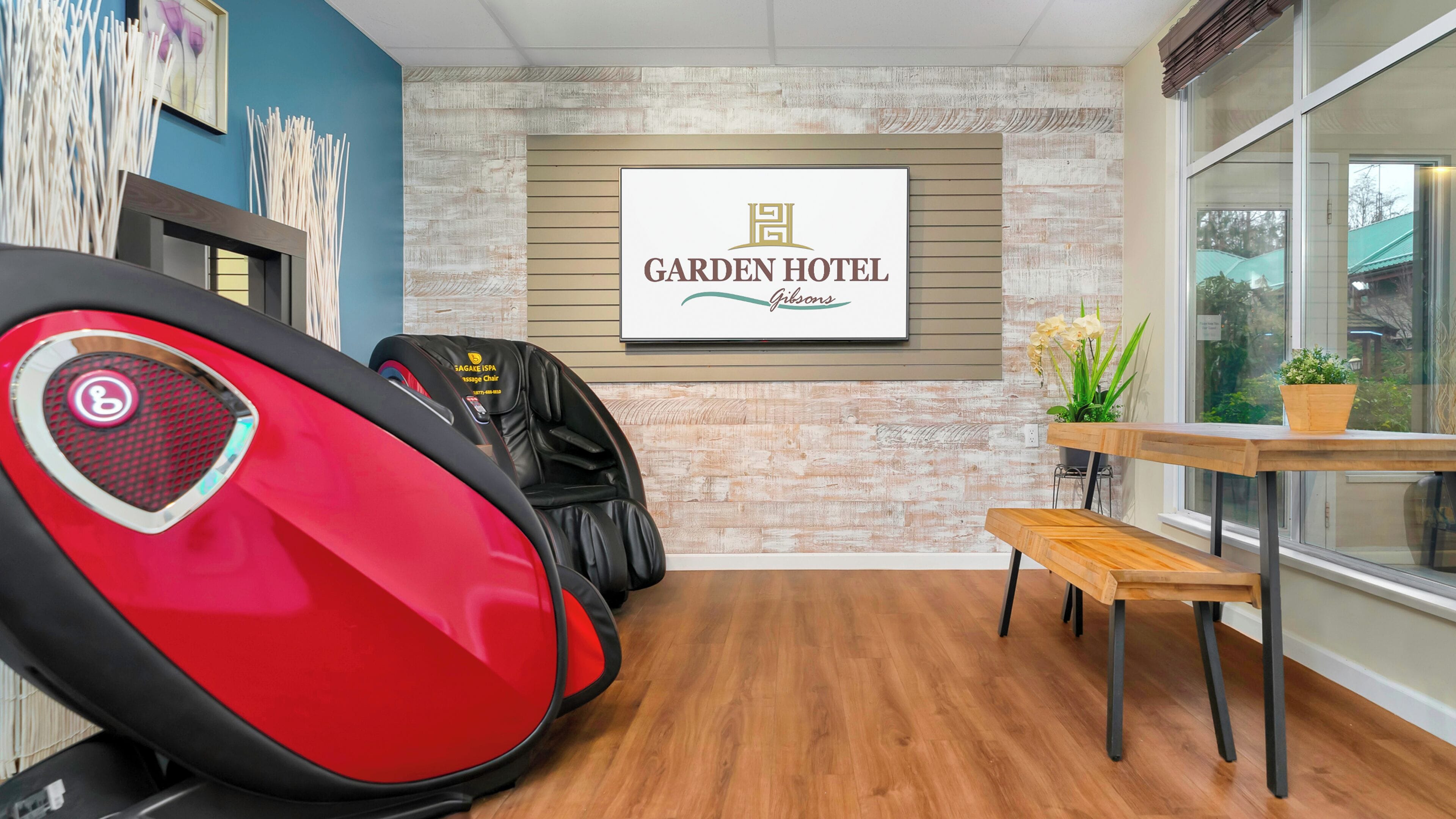 A room with a massage chair, a wooden bench, a potted plant, and a wall-mounted sign reading "Garden Hotel Gibbons".