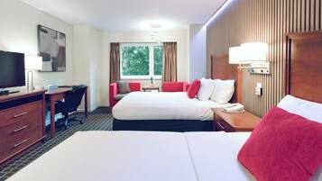 Quarto de hotel com cama, escrivaninha com cadeira, televisão e janela com cortinas.