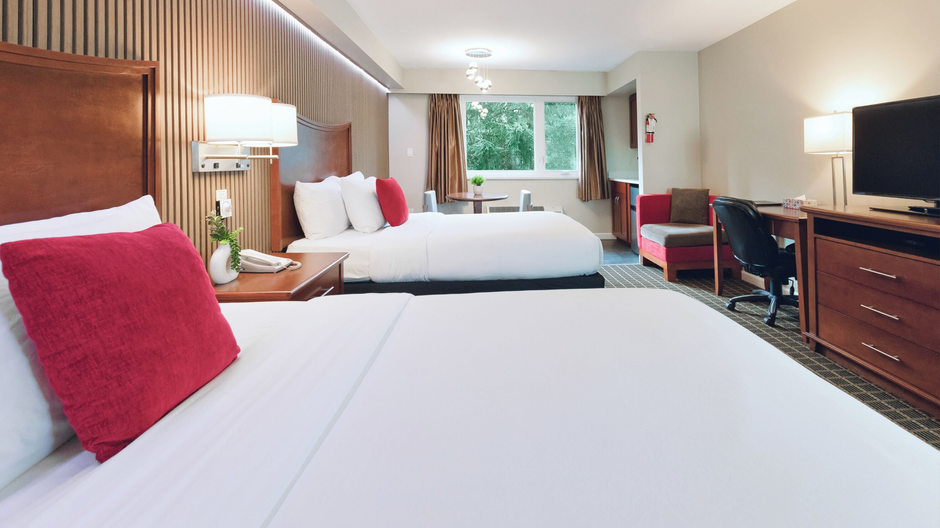 A hotel room with two beds, a desk, a chair, a TV, and a window with curtains.