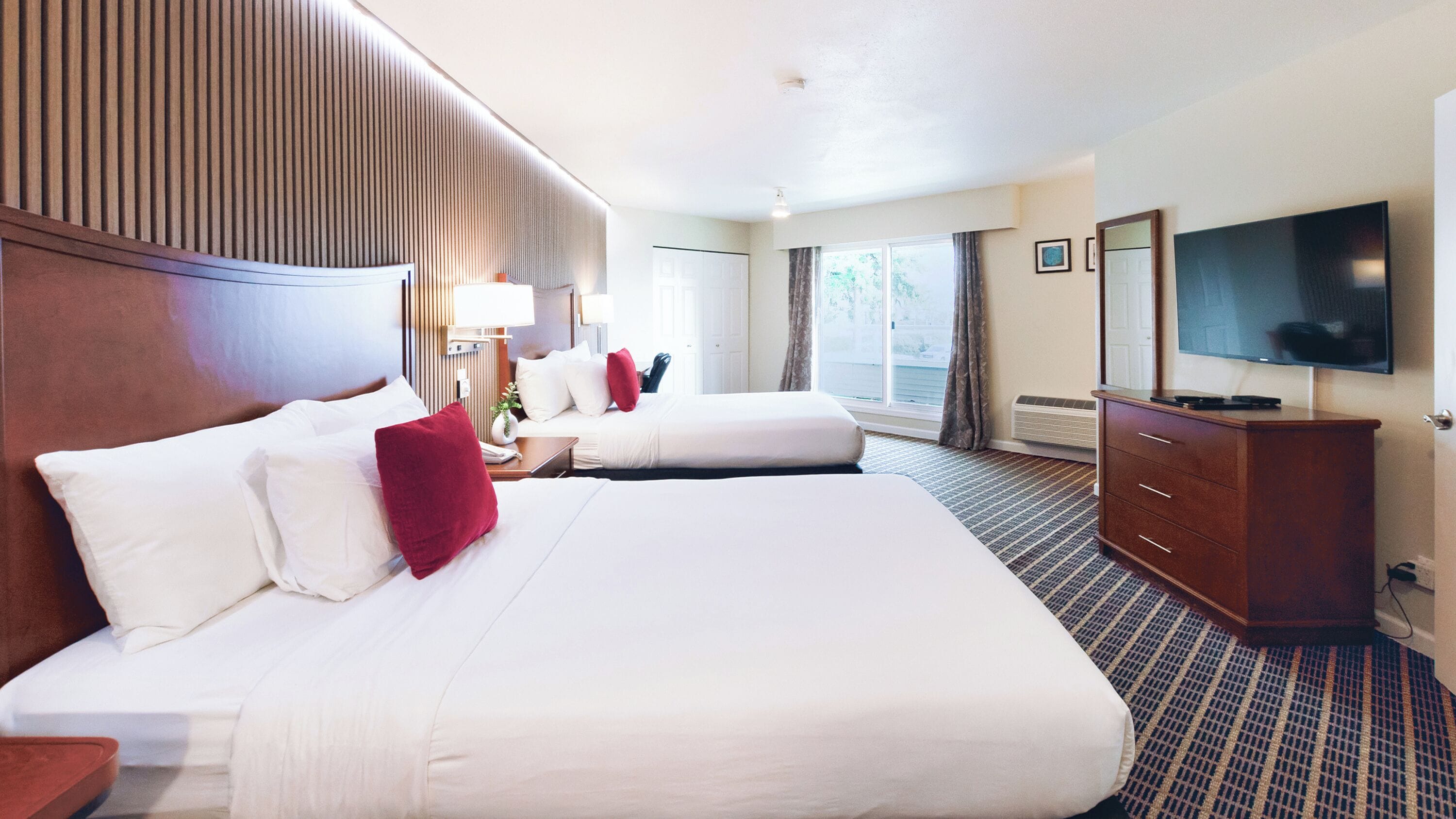A hotel room with two beds, a TV, a dresser, and a window with curtains.