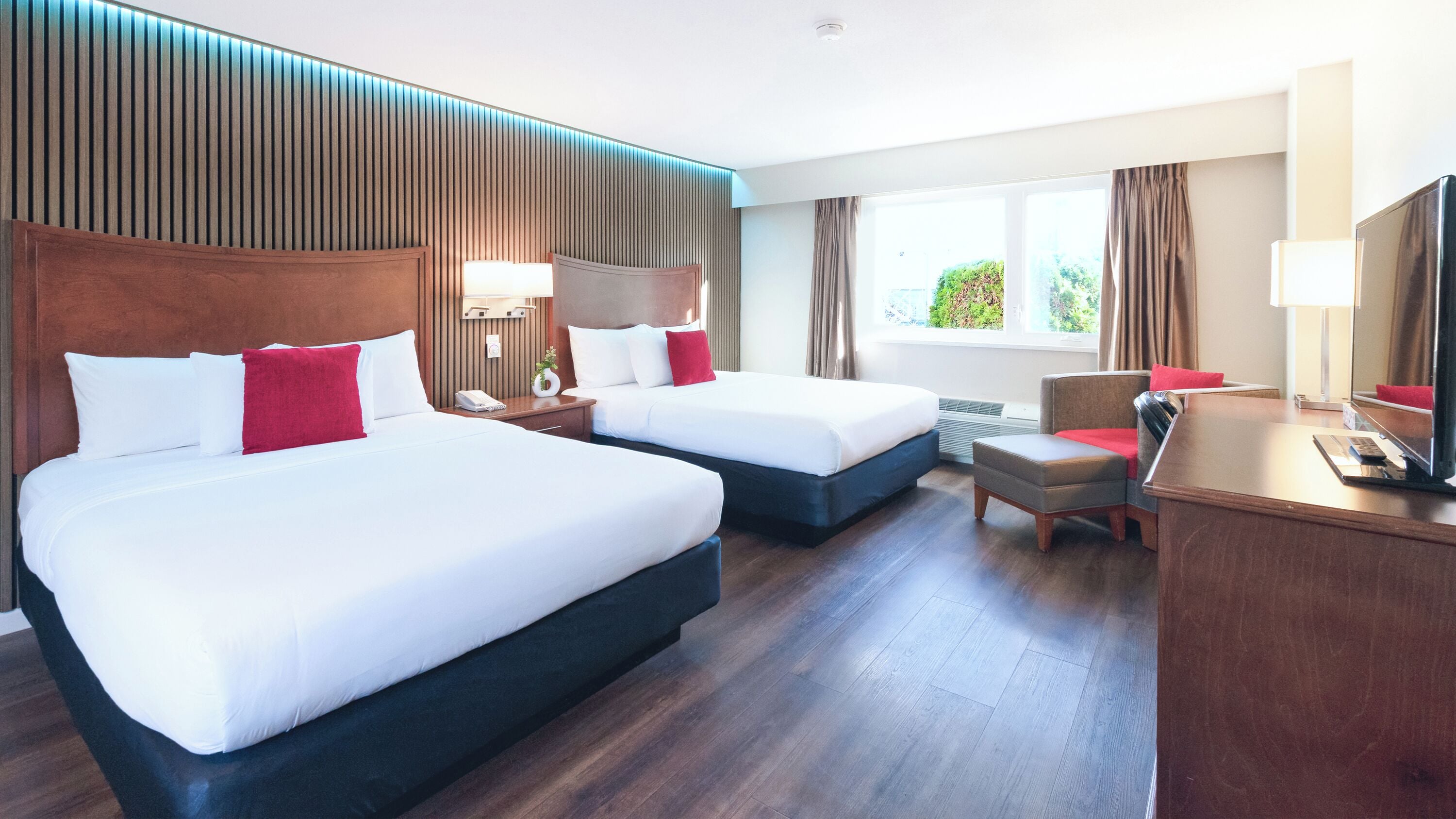 A hotel room with two beds, a desk, a chair, and a large window.