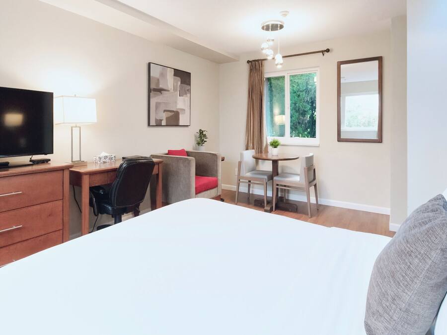 Ein Hotelzimmer mit einem Bett, einem Schreibtisch, einem Stuhl, einem Fernseher und einem Fenster mit Vorhängen.