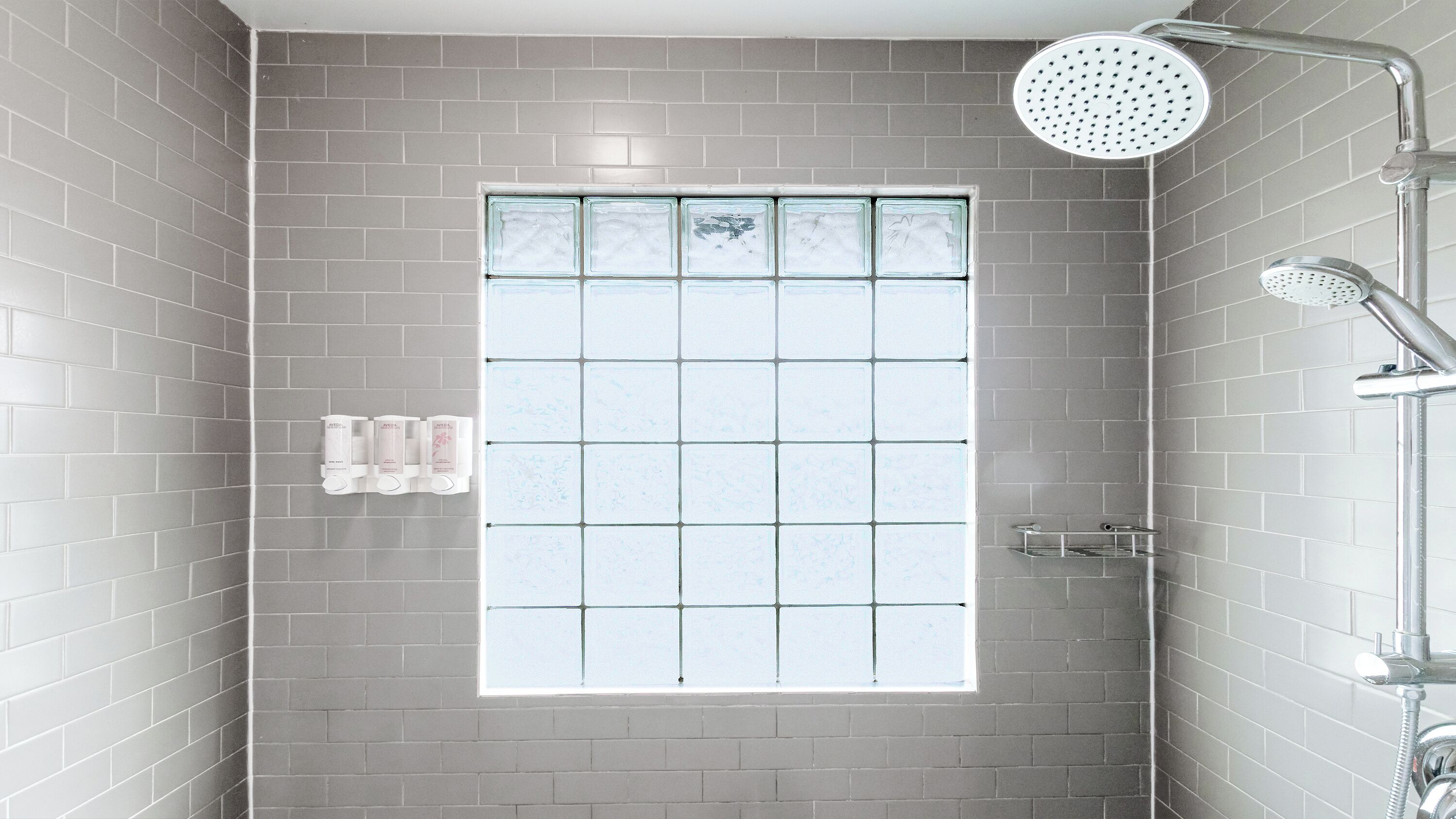 A shower area with a large window, grey tiled walls, and a showerhead.