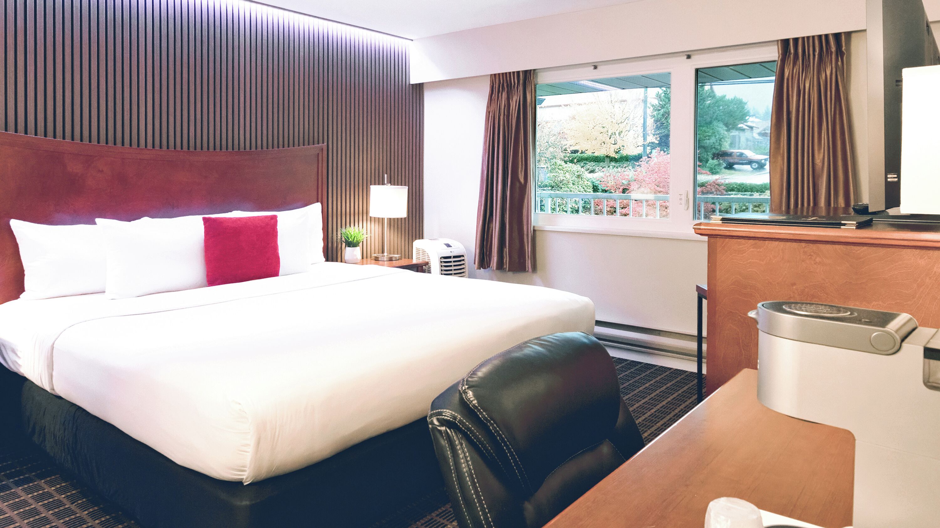 Habitación de hotel con una cama grande, un escritorio, una silla, un teléfono y una ventana con cortinas.