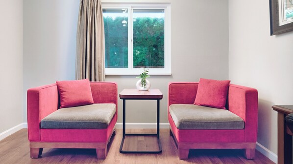 A room with two red sofas, a small table with a vase, and a window with curtains.