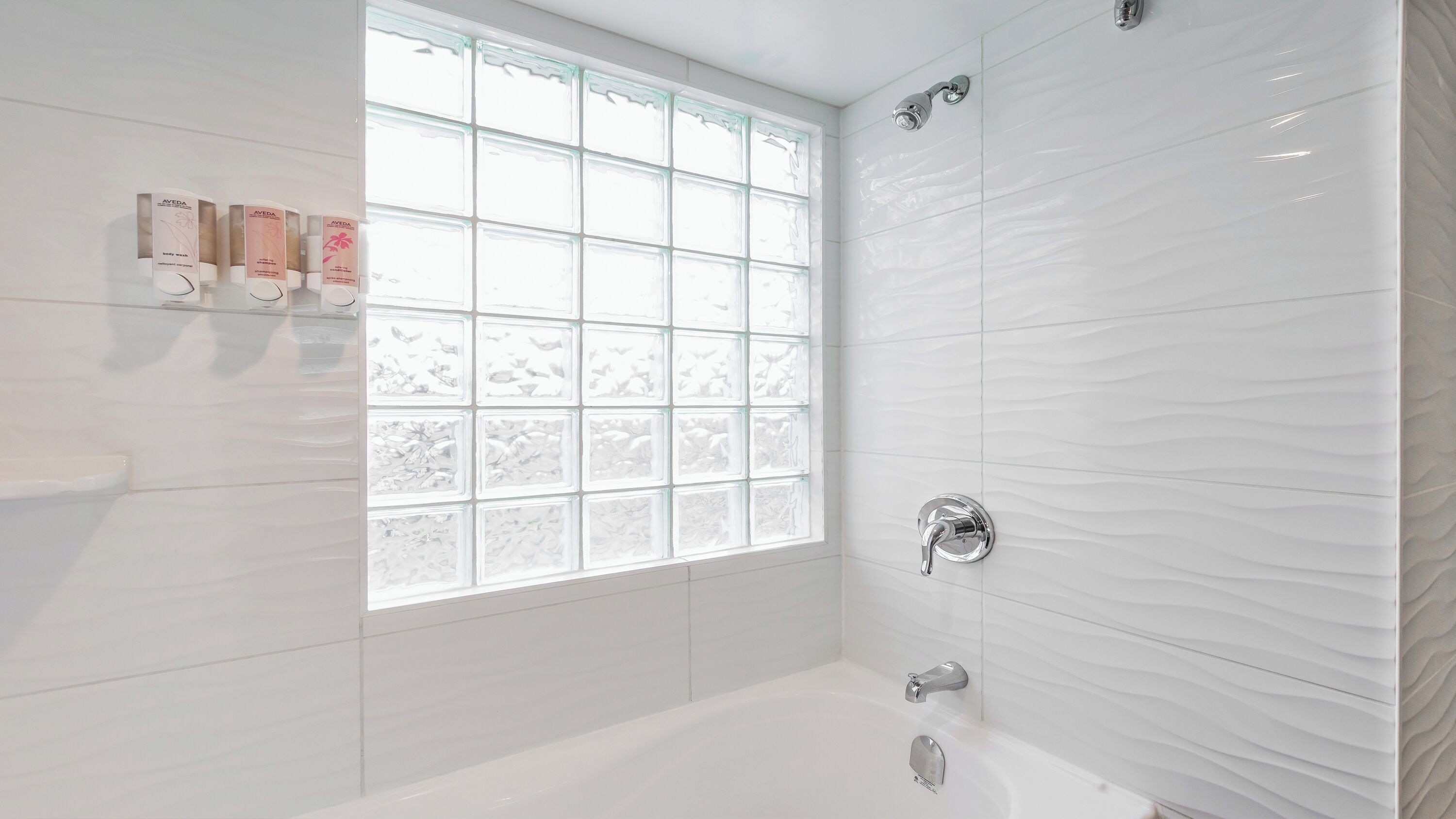 Un baño moderno con bañera, ventana con vidrio esmerilado y paredes cubiertas de azulejos blancos.