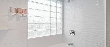 Un baño moderno con bañera, ventana con vidrio esmerilado y paredes cubiertas de azulejos blancos.