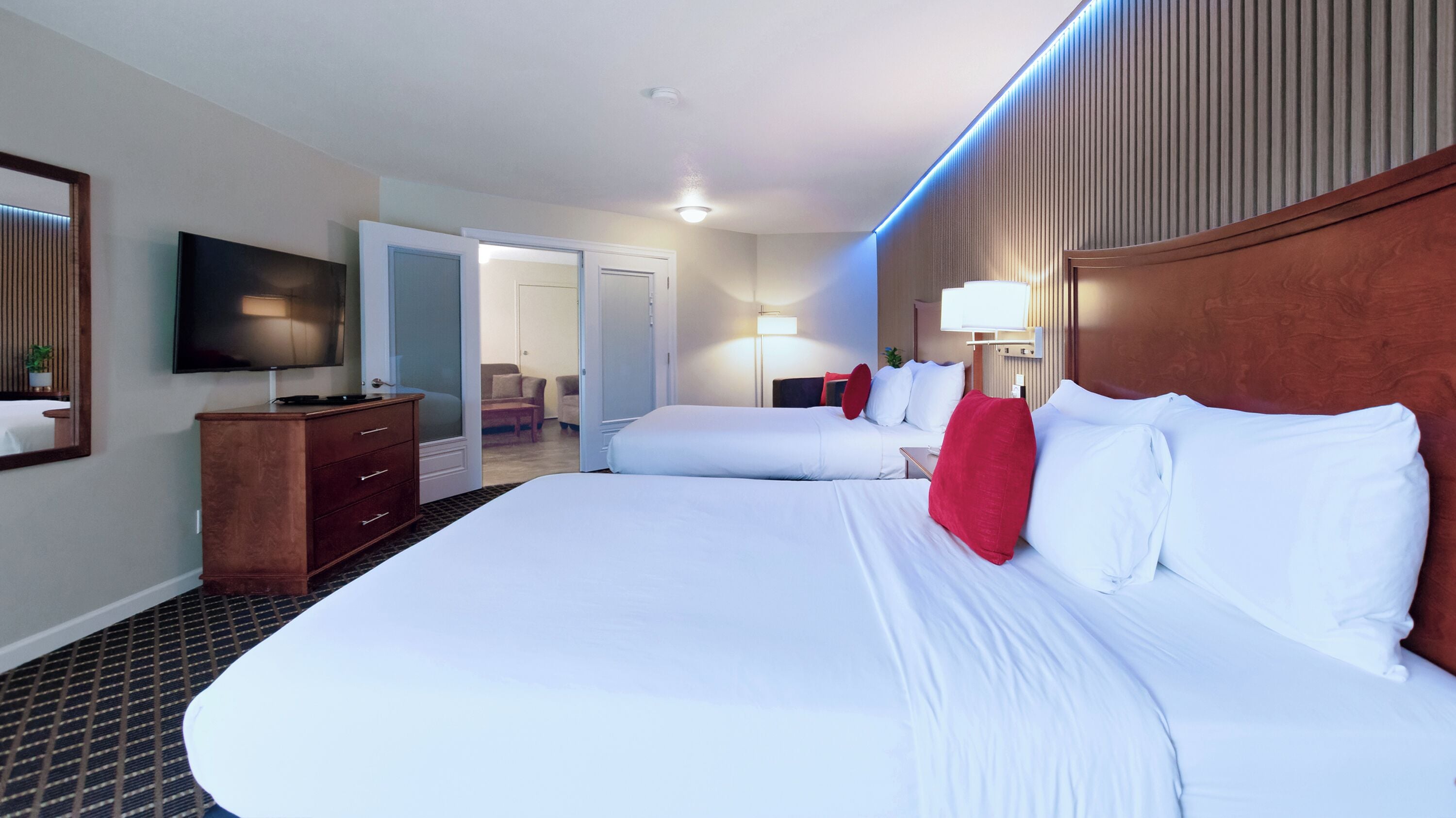 A hotel room with two beds, a TV, a dresser, and a door leading to another room.