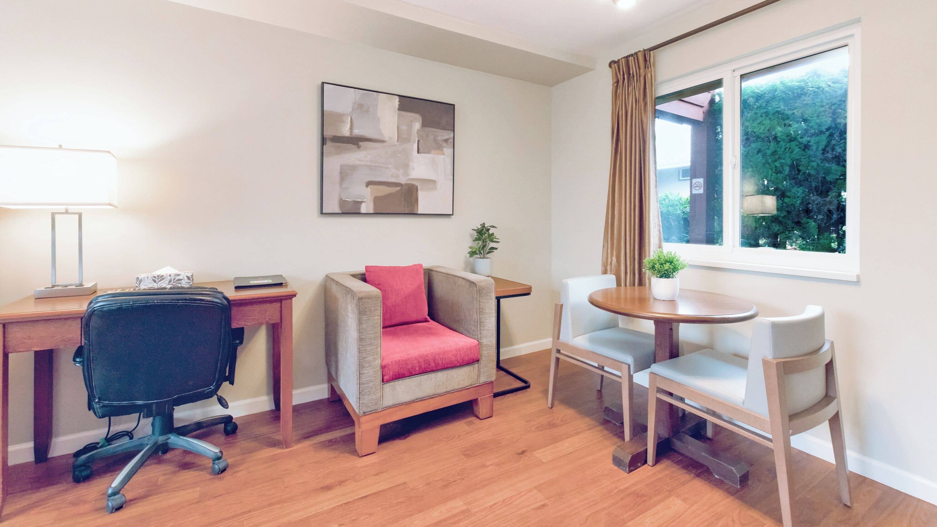 Ein modernes Zimmer mit Schreibtisch, Bürostuhl, Sofa und einem kleinen Esstisch mit Stühlen.