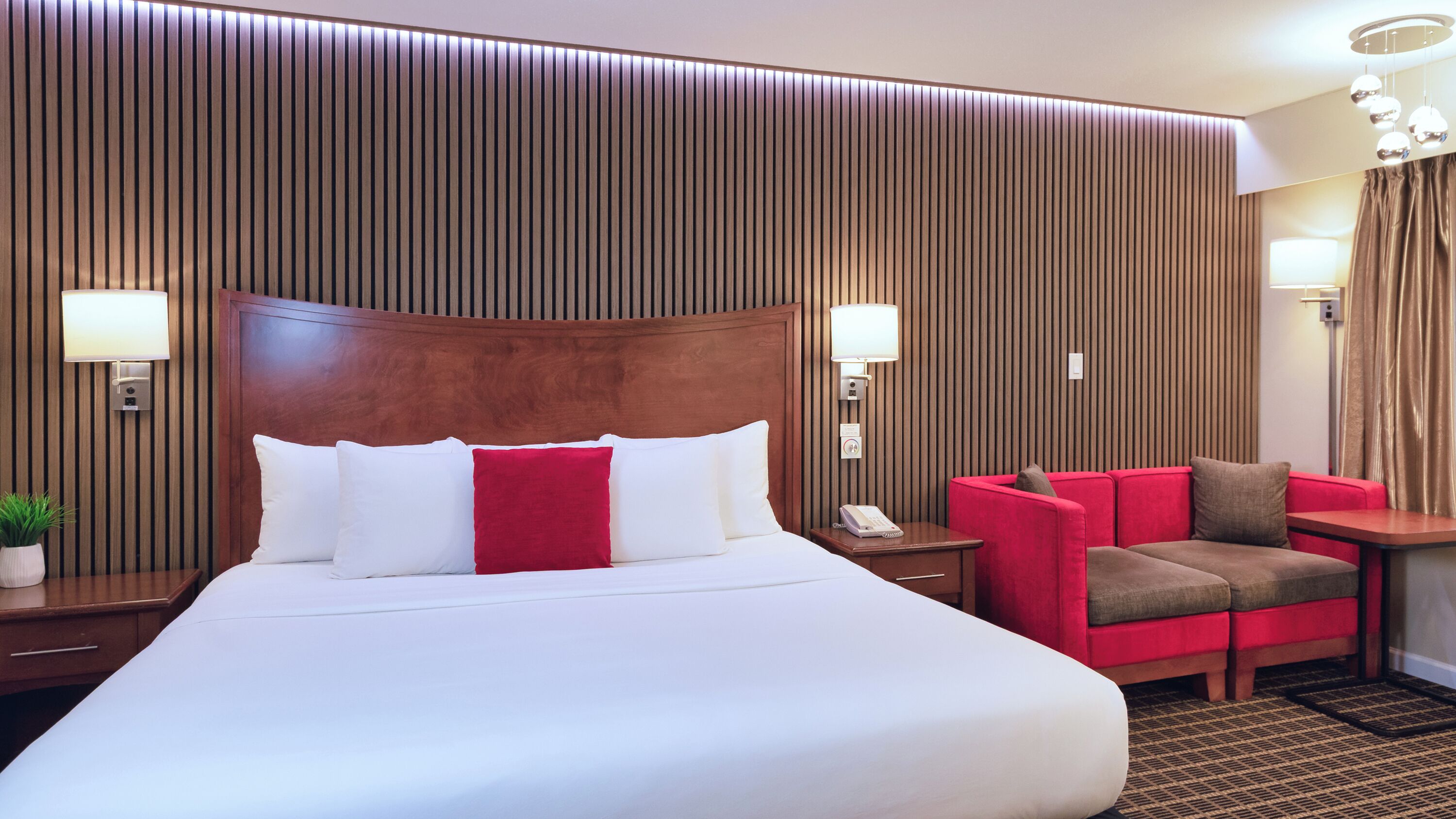 A hotel room with a large bed, a red sofa, and two wall-mounted lamps.
