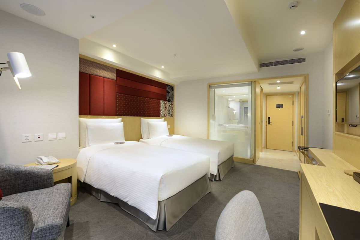 Une chambre d’hôtel avec deux lits, un bureau, une chaise et une armoire.