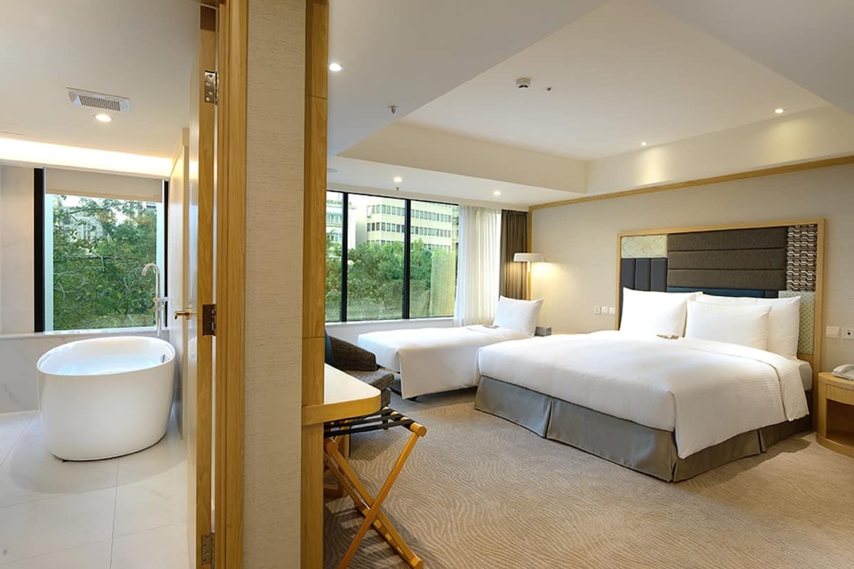 Une chambre d’hôtel moderne avec un grand lit, deux petits lits, une baignoire et un bureau.