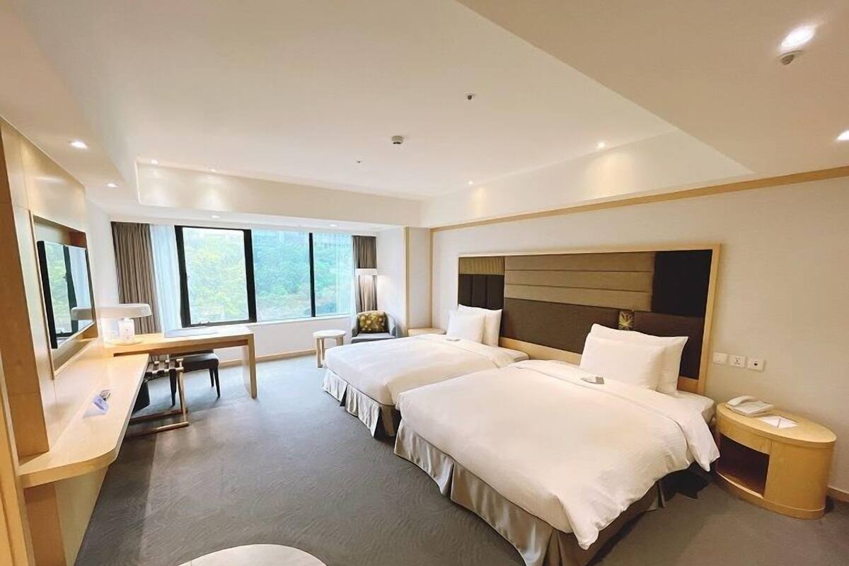 Een hotelkamer met twee bedden, een bureau, een stoel, een nachtkastje en een groot raam.