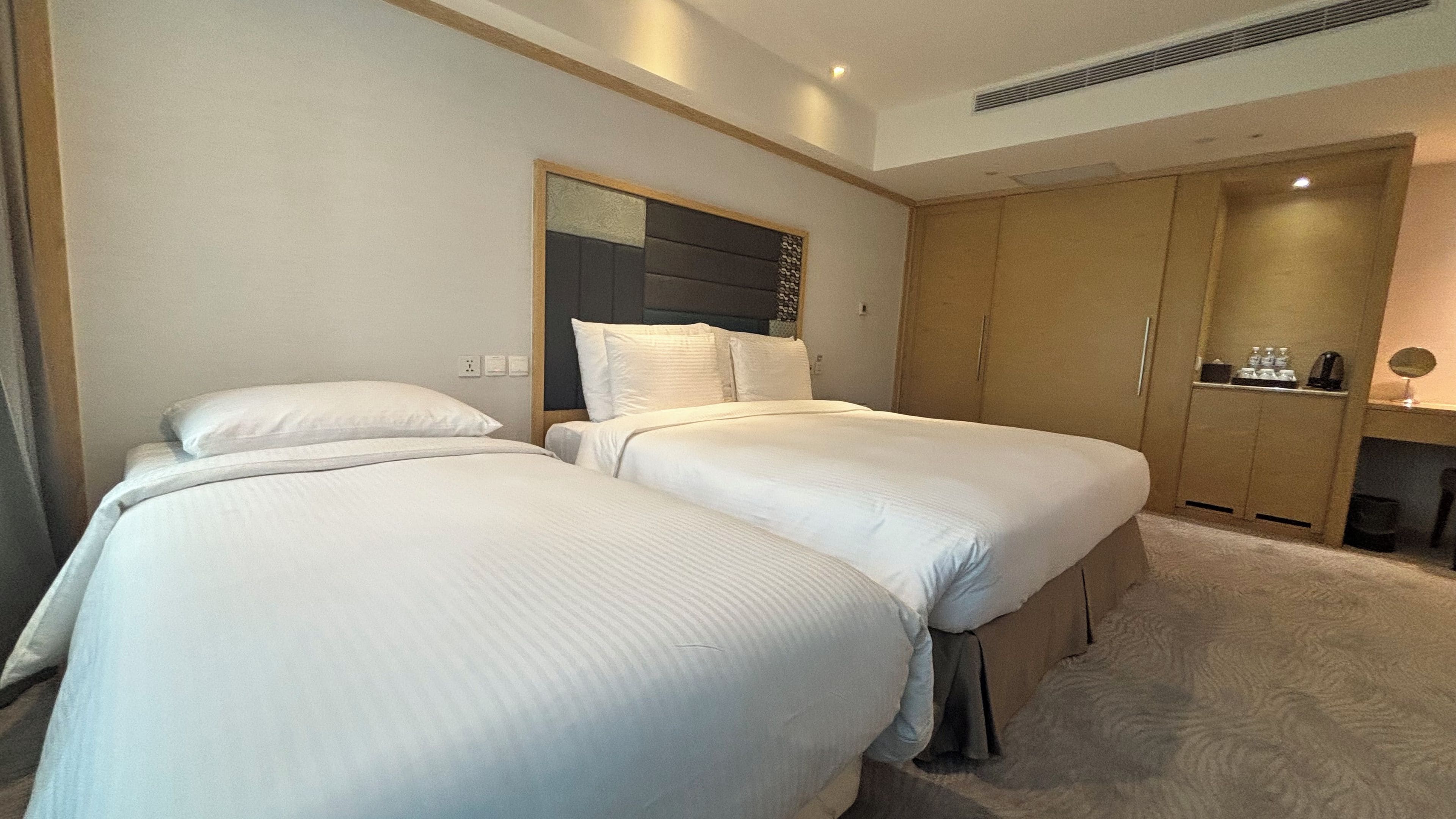 Habitación de hotel con dos camas, un armario y un escritorio pequeño con espejo.