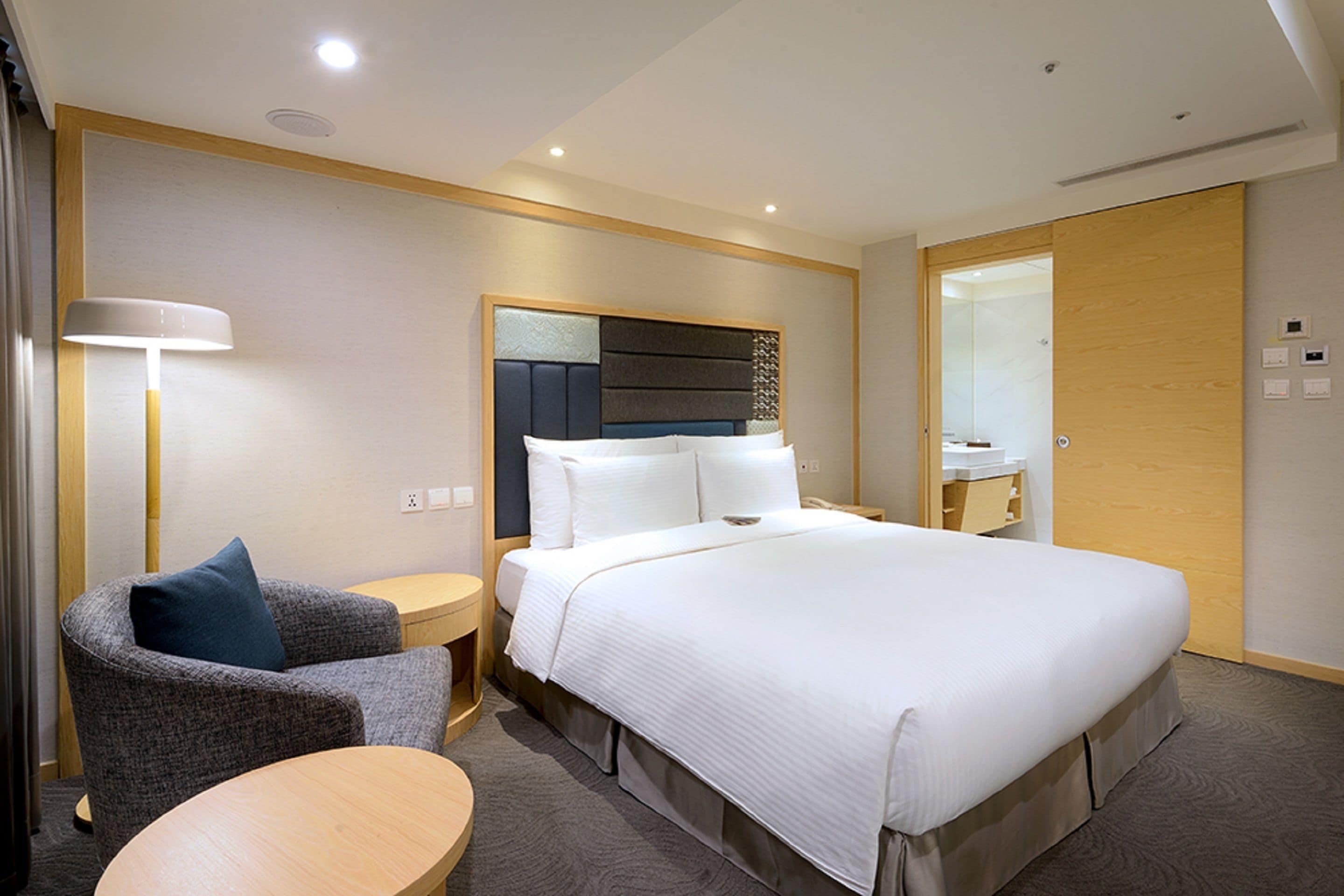 Une chambre d’hôtel avec un grand lit, une chaise, une petite table et un miroir.