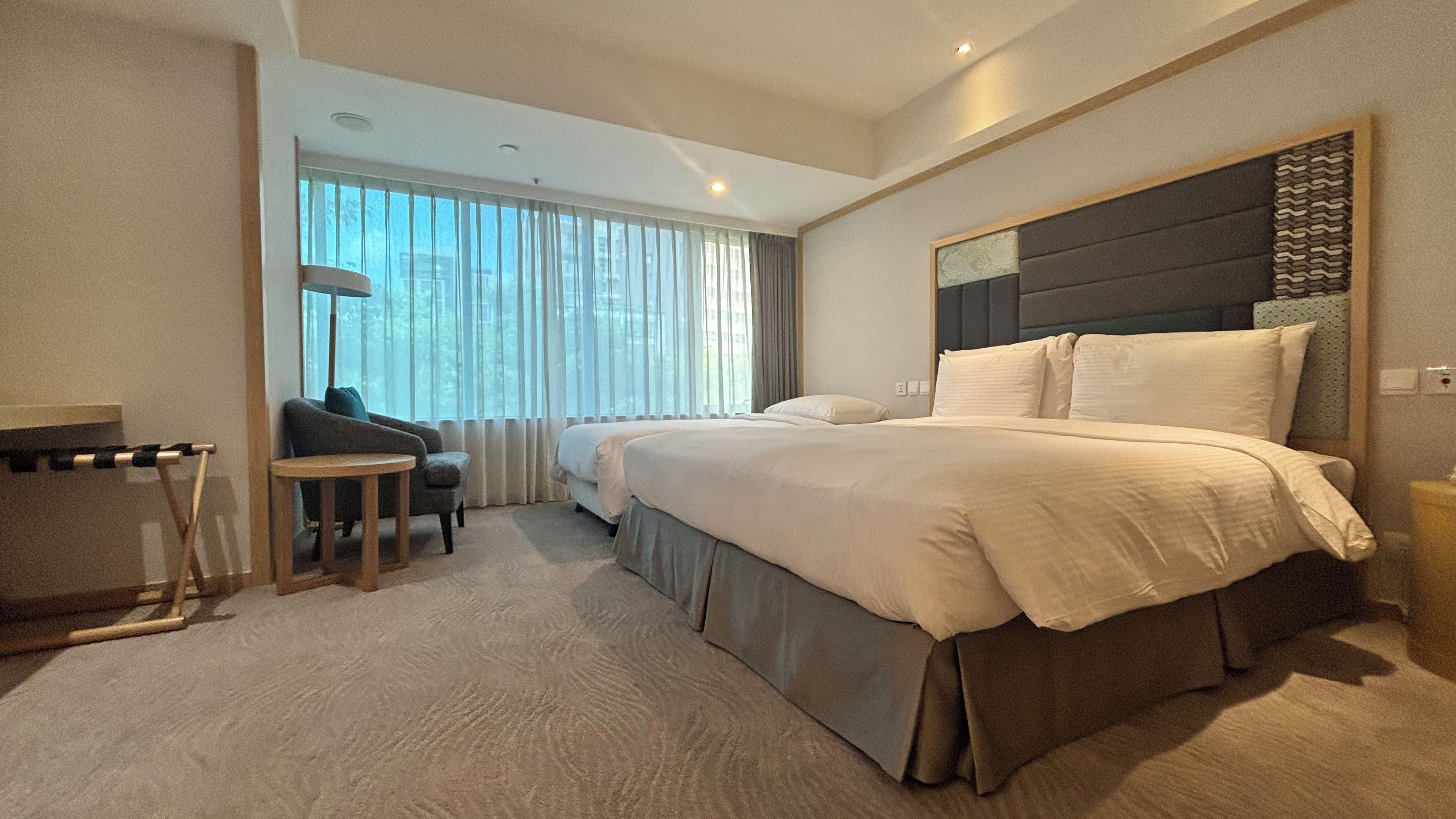A hotel room with a large bed, a desk, a chair, and a view of the outdoors through the window.