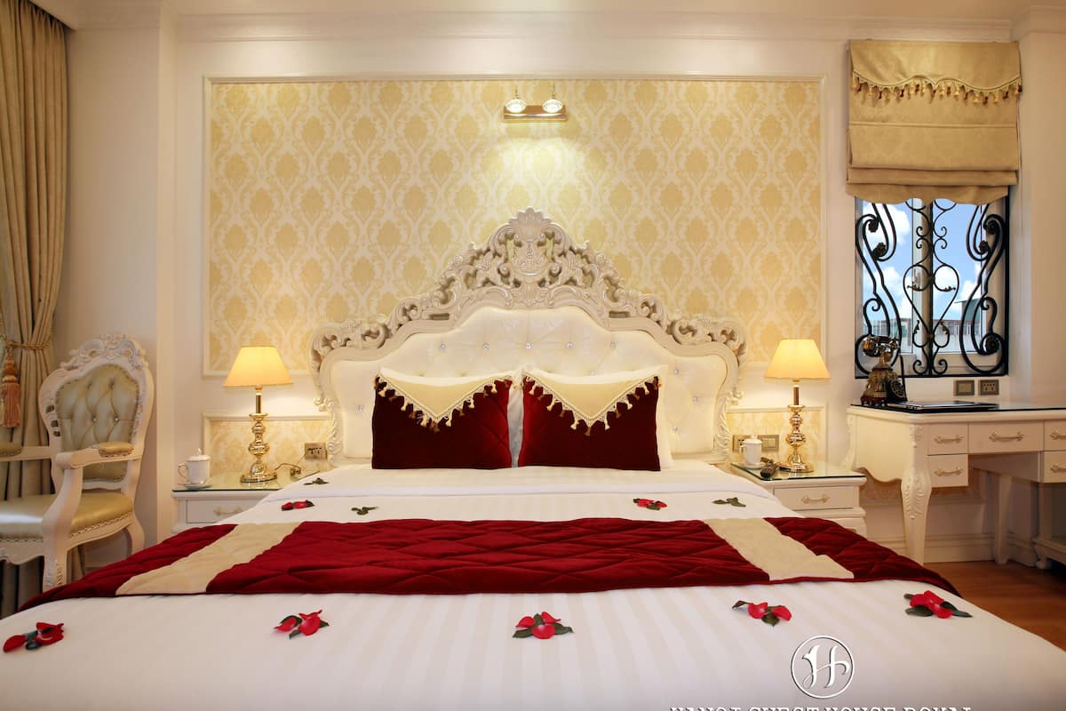 A luxurious hotel room with a large bed, ornate headboard, and elegant decor.