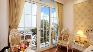 Une pièce dotée d’une grande porte-fenêtre coulissante donnant sur un balcon, d’un fauteuil moelleux, d’une table de chevet avec une lampe et d’un panneau décoratif mural.