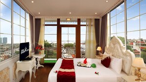 Une chambre d’hôtel avec un grand lit, une télévision, un balcon donnant sur la ville et une fenêtre avec des rideaux.