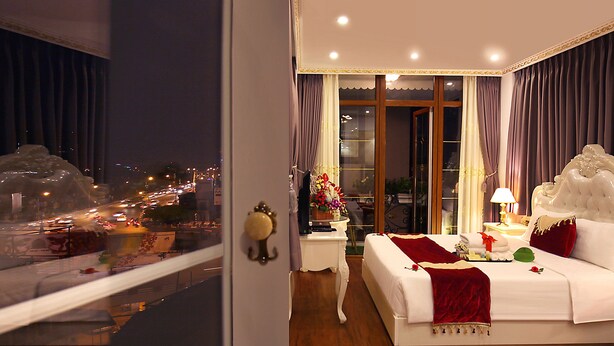 Une chambre d’hôtel avec un grand lit, une table de chevet, une lampe et une vue sur le paysage urbain par la fenêtre.