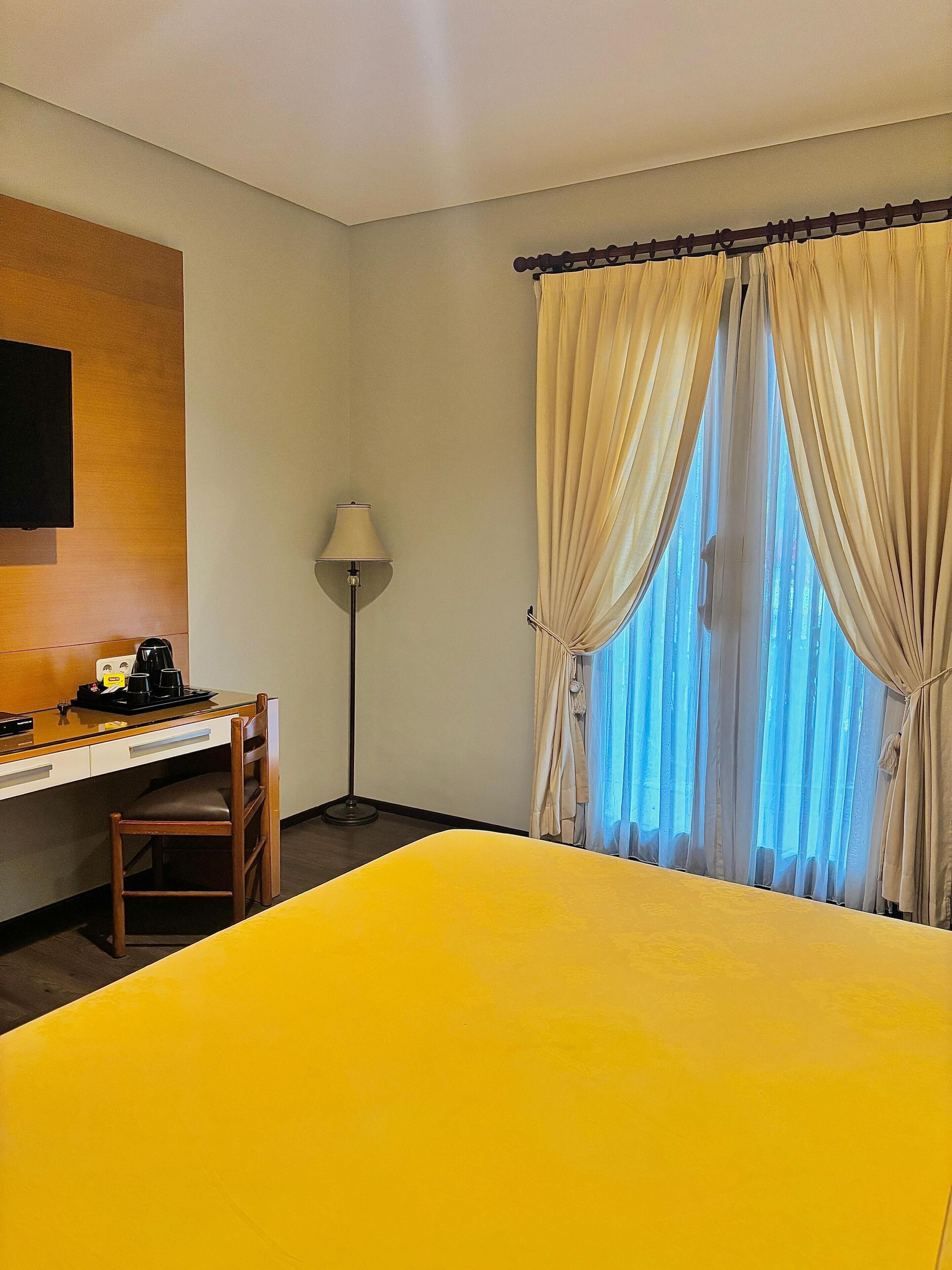 Une chambre d’hôtel avec un lit, un bureau avec une chaise, une lampe et des rideaux.