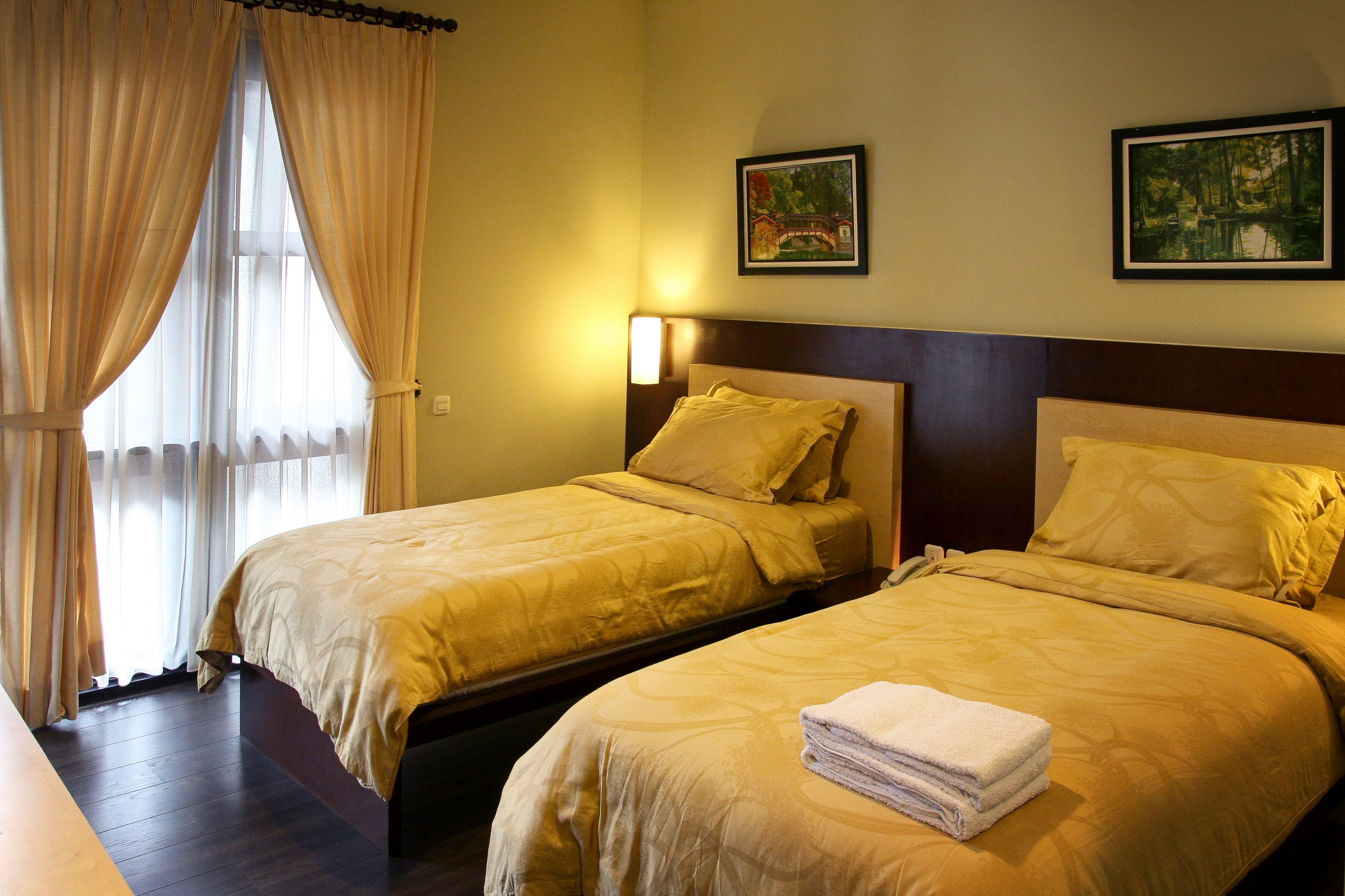 Une chambre d’hôtel avec deux lits, une fenêtre avec des rideaux et deux tableaux encadrés accrochés au mur.